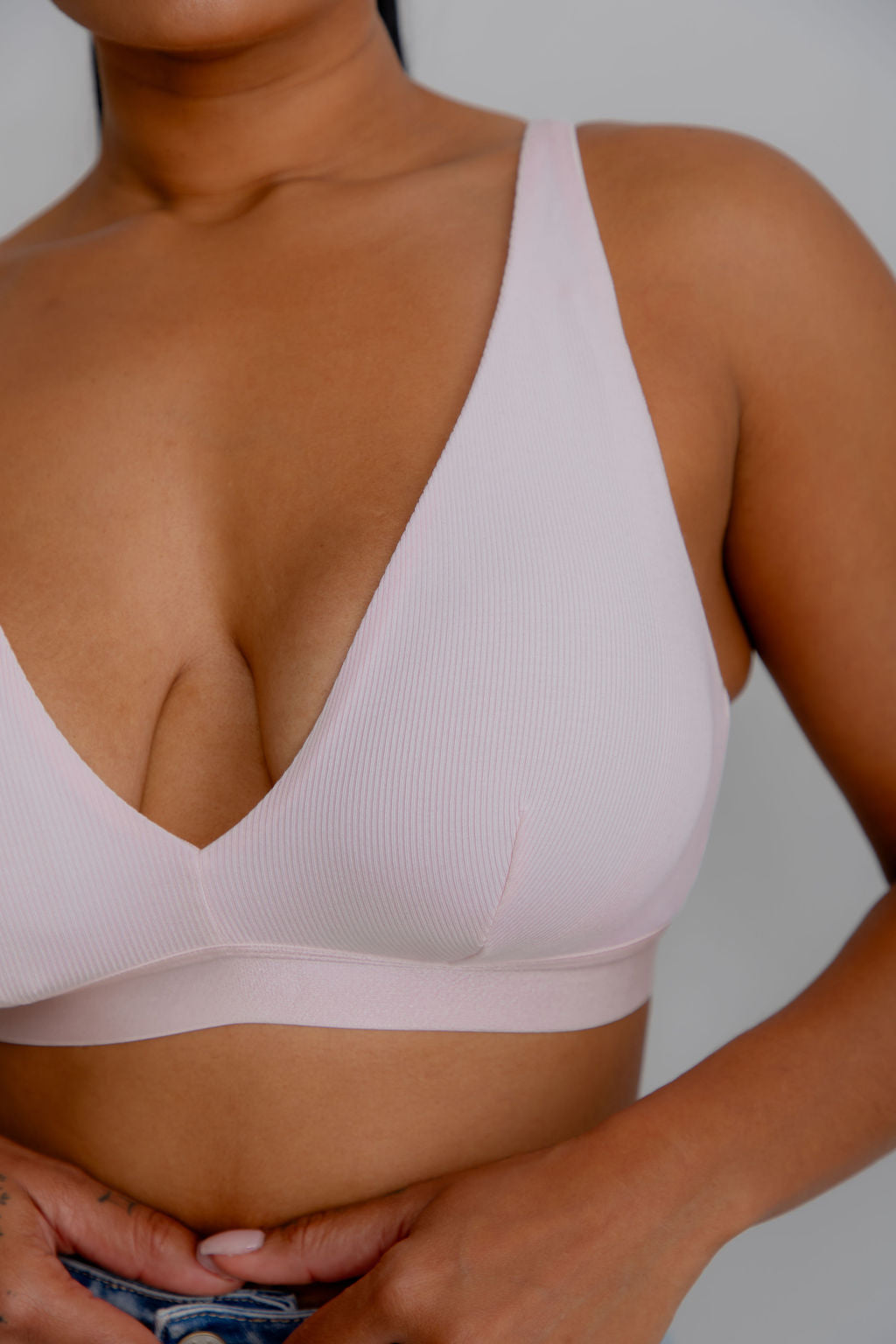 Close-up of a model wearing a light pink ribbed wireless bra with a deep V-neck and wide underband, shown against a neutral gray background.