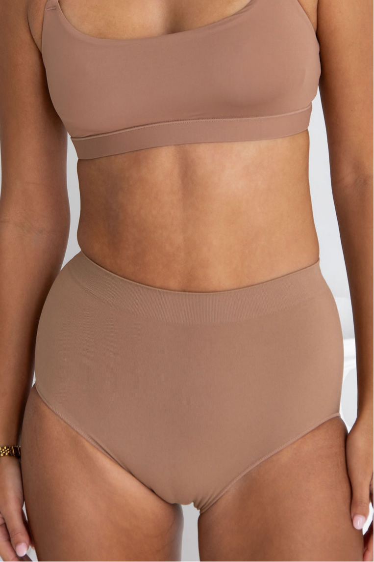 Person wearing a brown sports bra and high-waisted underwear set on a neutral background