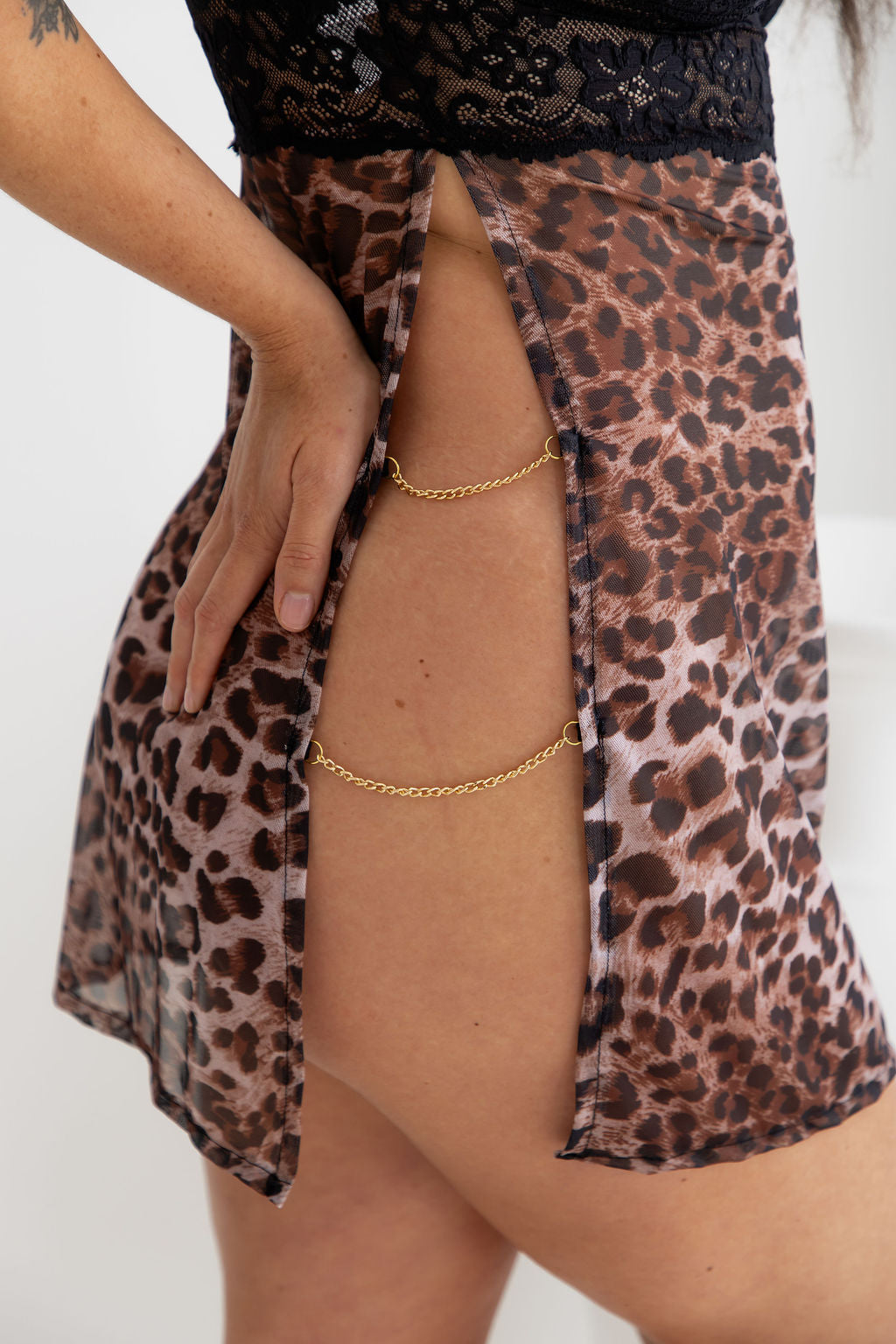 Person wearing a leopard print skirt with a gold anklet on a white background